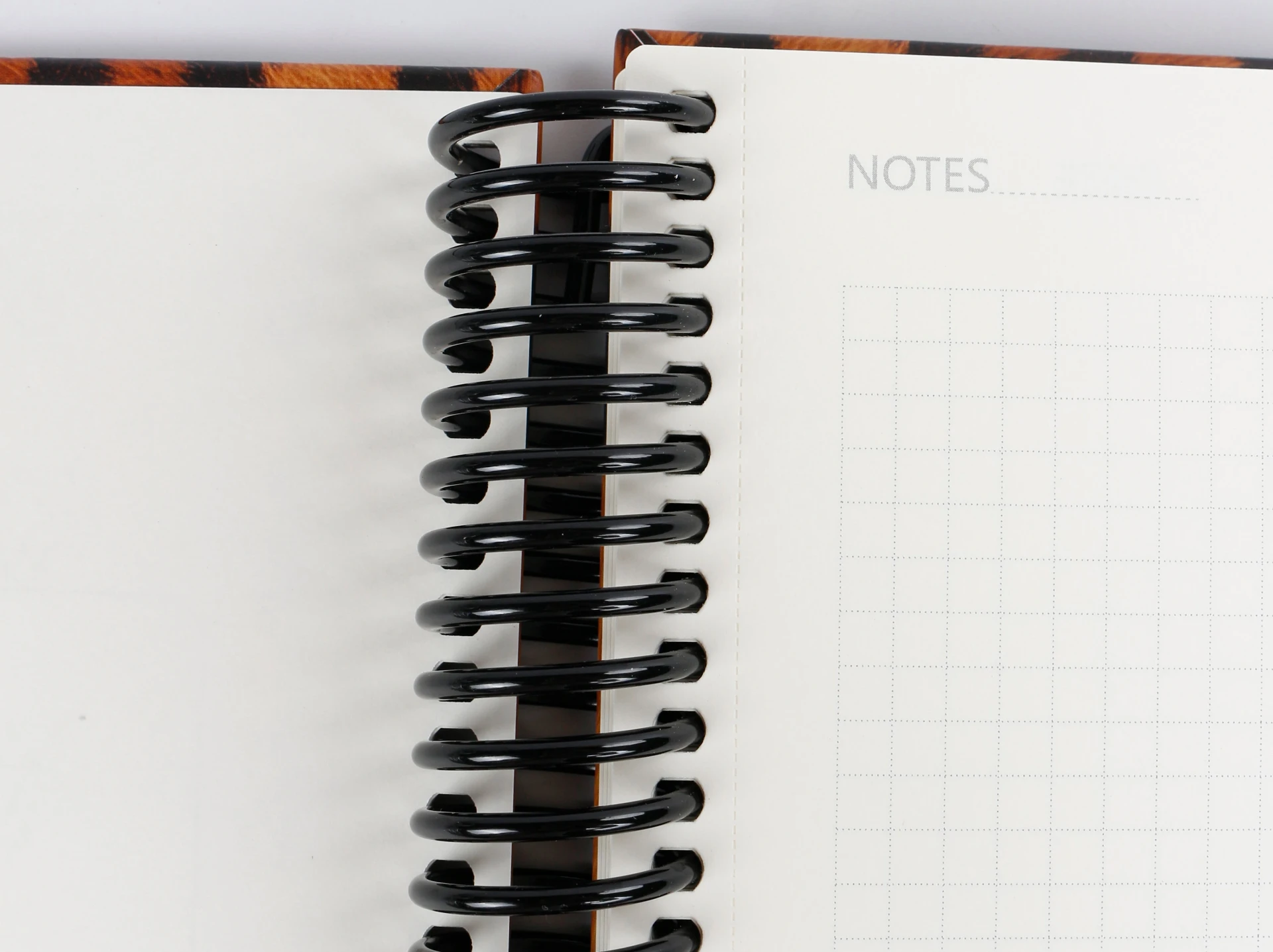 Black PET plastic spiral coil binding on an open tiger-stripe notebook Black PET plastic spiral coil binding on an open tiger-stripe notebook